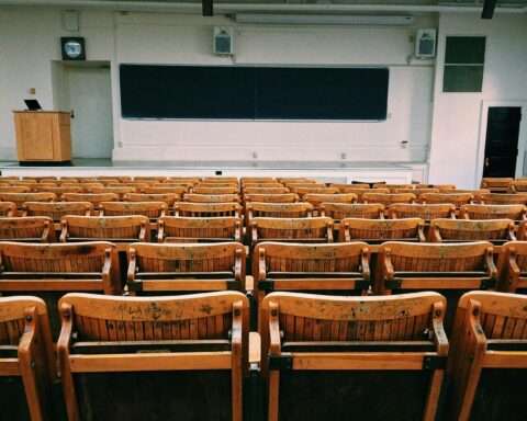 A university classroom with wooden chairs before a black chalkboard.