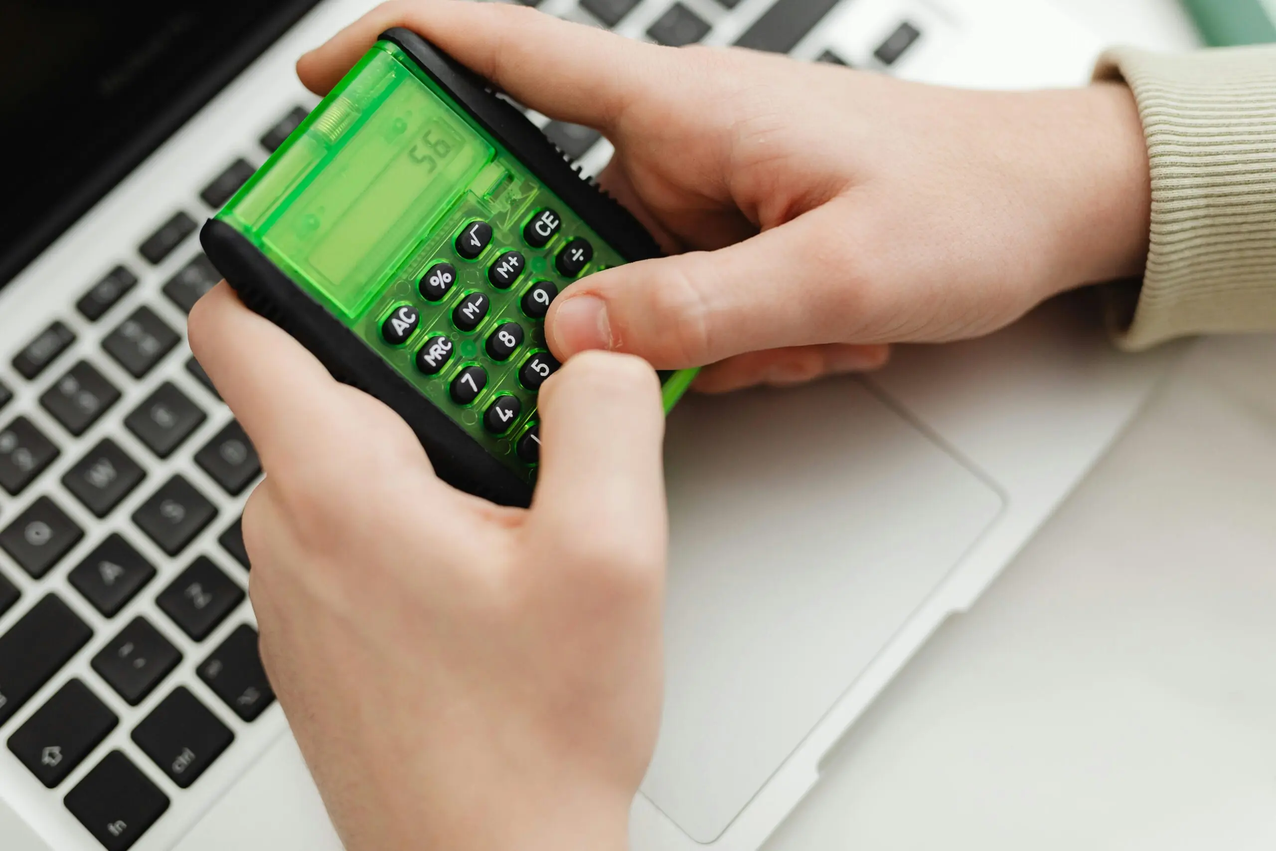 A pair of hands types on a calculator before a laptop.