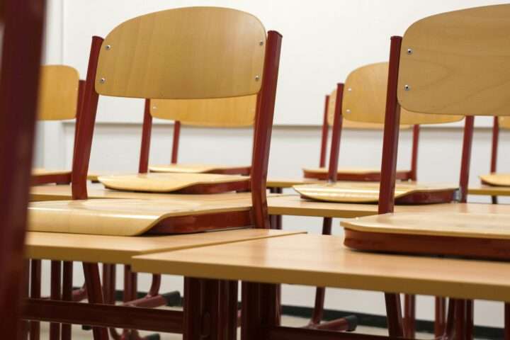 Class chairs in a school classroom before a whiteboard and white wall.