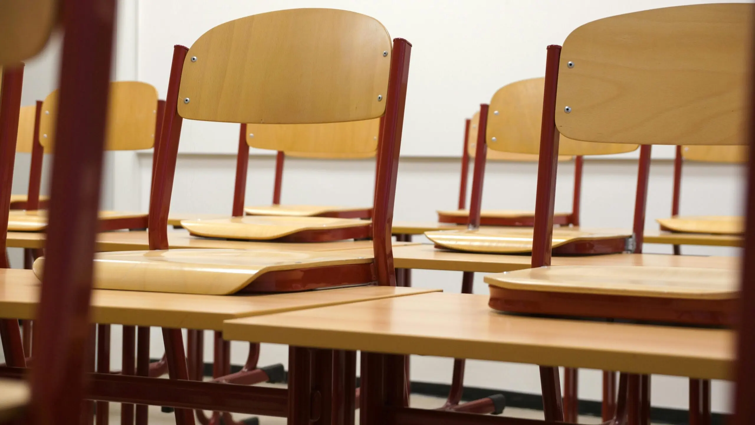 Class chairs in a school classroom before a whiteboard and white wall.
