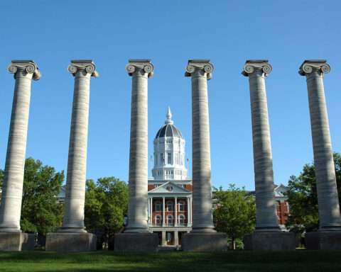 Six pillars stand tall before Jesse Hall and a blue sky at the University of Missouri.