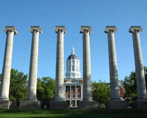 Six pillars stand tall before Jesse Hall and a blue sky at the University of Missouri.
