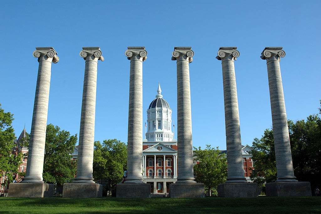 Six pillars stand tall before Jesse Hall and a blue sky at the University of Missouri.