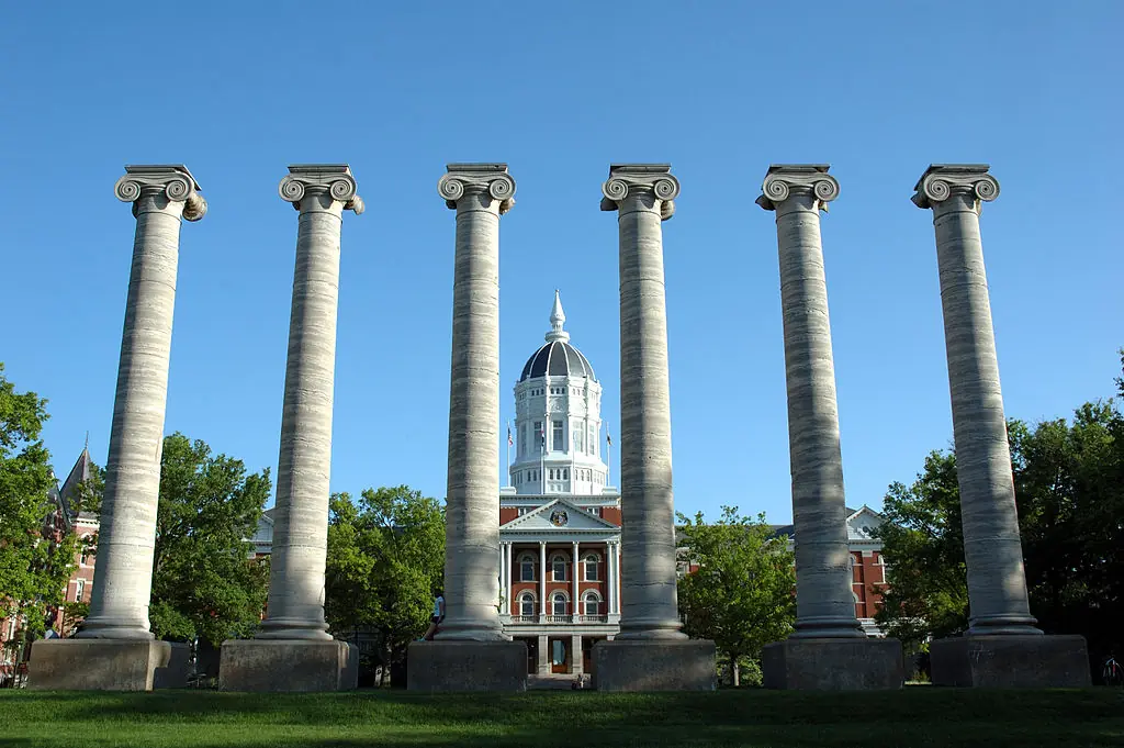 Six pillars stand tall before Jesse Hall and a blue sky at the University of Missouri.