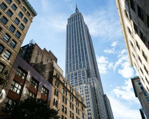 A New York City sky scrapper from the ground before a cloudy blue sky.