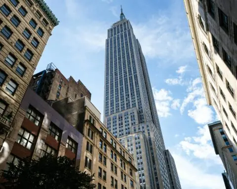 A New York City sky scrapper from the ground before a cloudy blue sky.