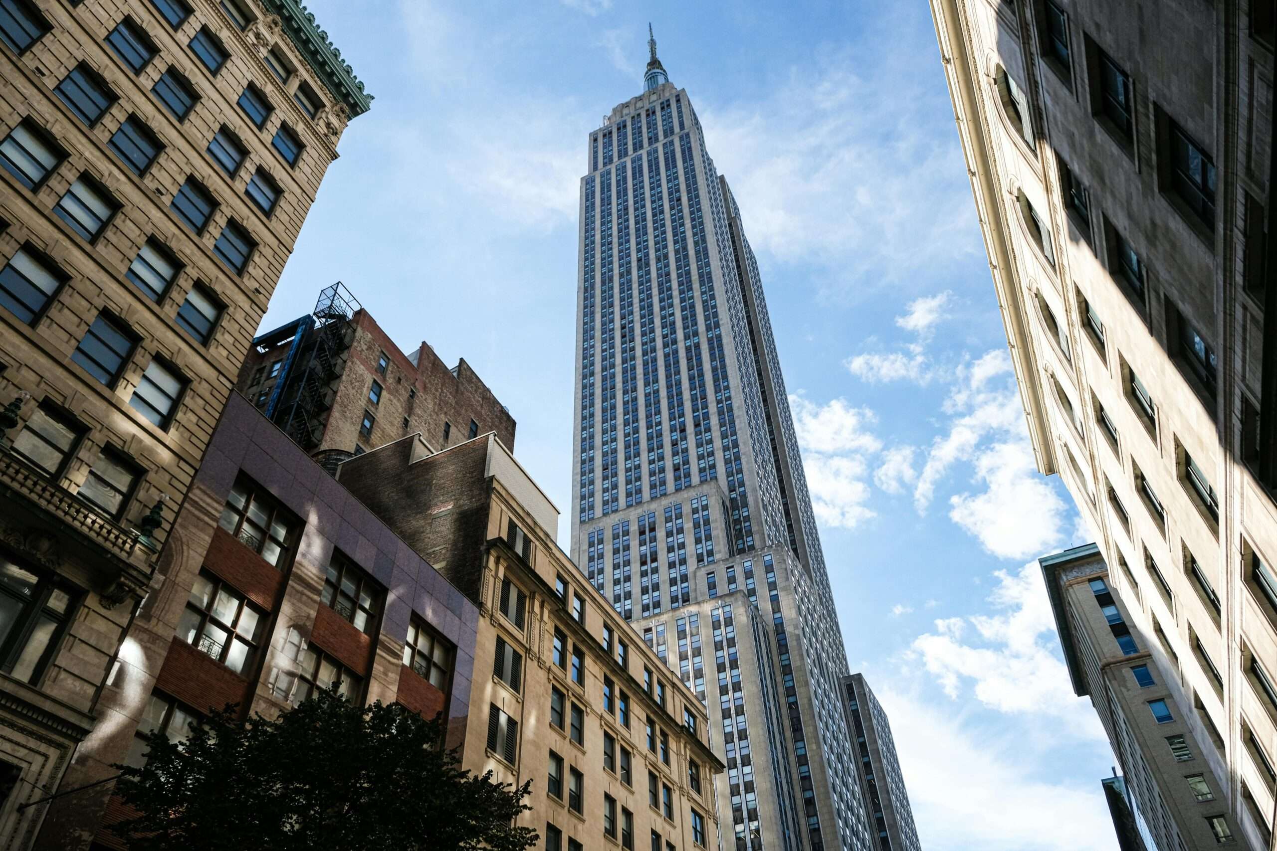 A New York City sky scrapper from the ground before a cloudy blue sky.