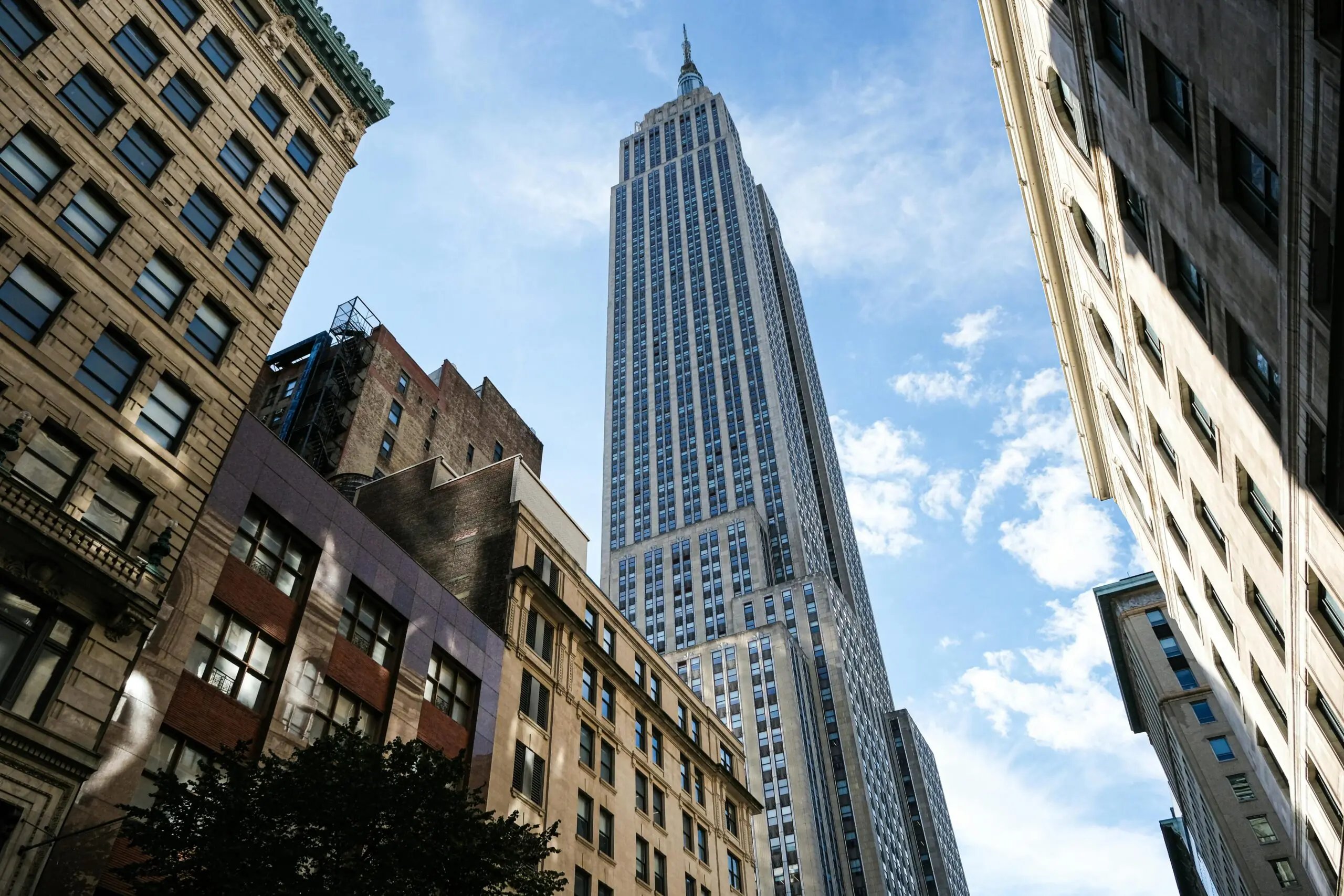 A New York City sky scrapper from the ground before a cloudy blue sky.