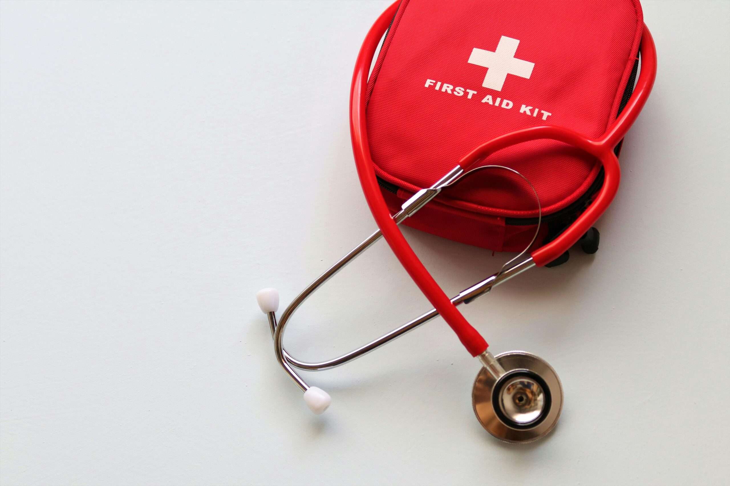 A red first aid kit and a stethoscope against a white table.