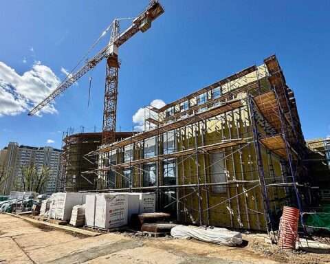 A crane and a partially developed school on a construction site before a clear blue sky.