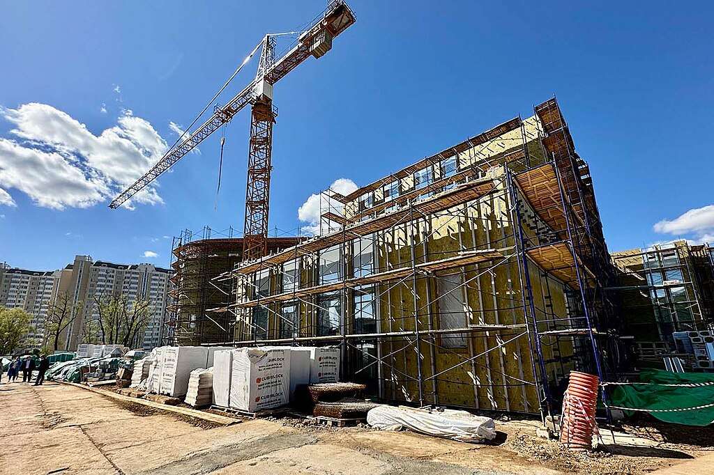 A crane and a partially developed school on a construction site before a clear blue sky.