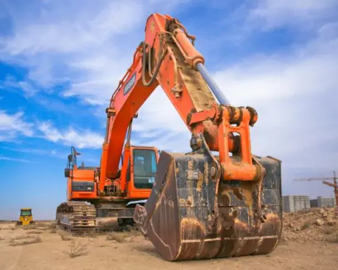 An orange excavator before a blue sky and a dirt mound.