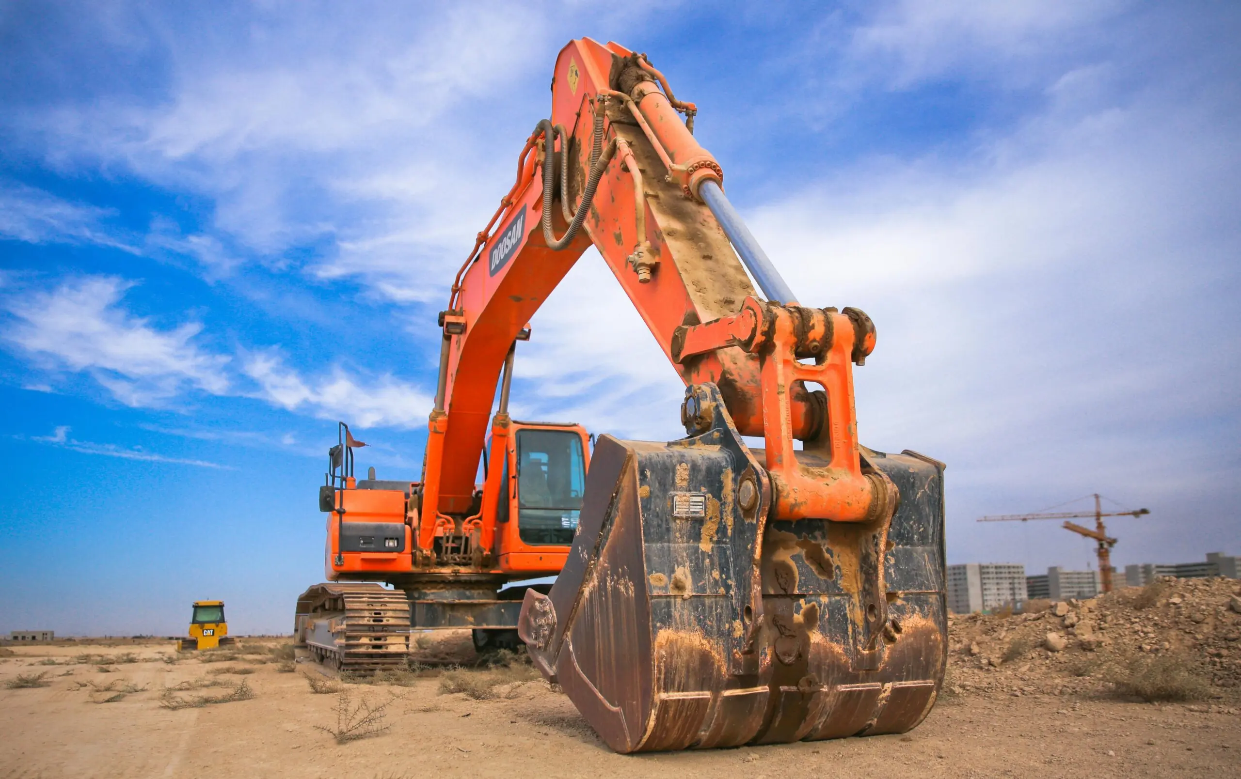 An orange excavator before a blue sky and a dirt mound.