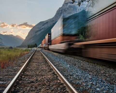 A moving train passes through a mountain corridor along rail tracks.