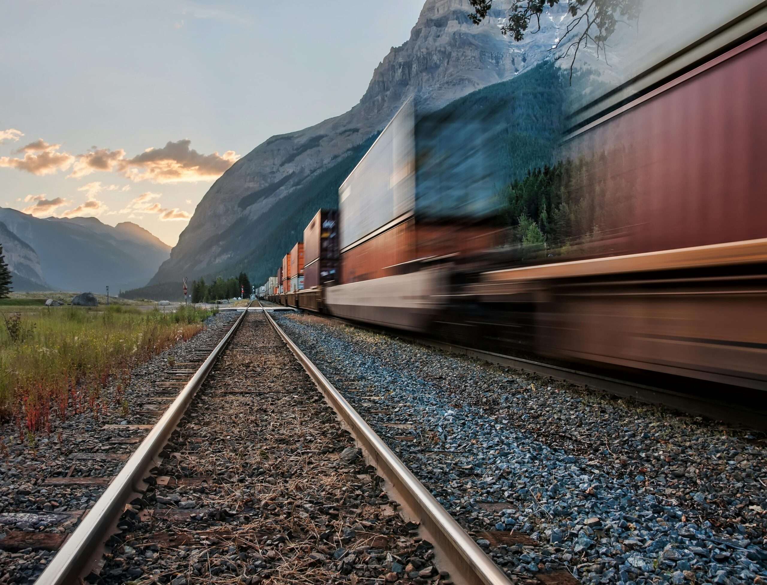 A moving train passes through a mountain corridor along rail tracks.
