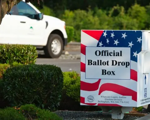 A red, white and blue ballot box before green grass and a parked car.