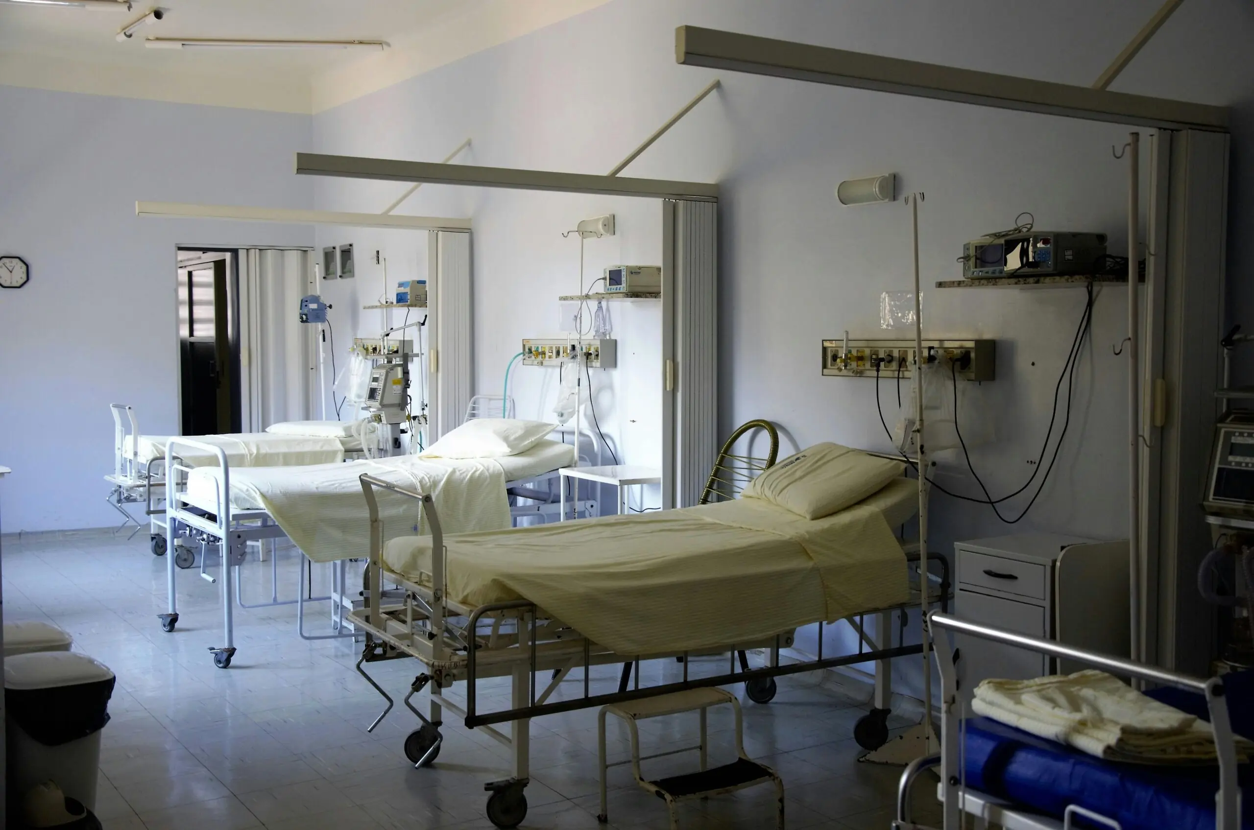 A hospital room with several lined up beds.