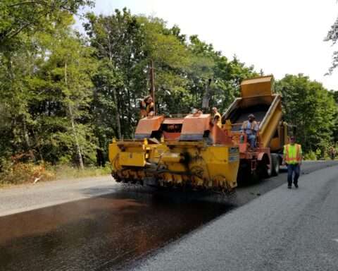 A roller machine rolls over freshly laid asphalt.