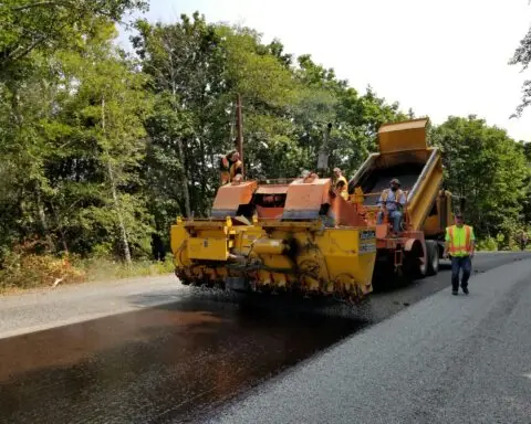 A roller machine rolls over freshly laid asphalt.