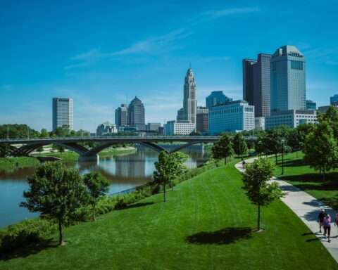 A view of the Columbus skyline in Ohio from a green park near a water feature.