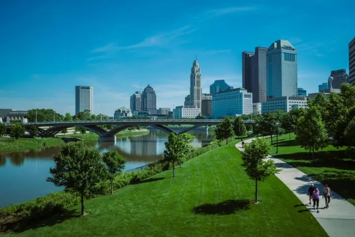 A view of the Columbus skyline in Ohio from a green park near a water feature.