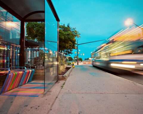A bus zooms past a bus station with a multi-colored bench.