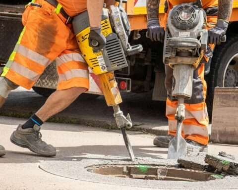 Construction workers use jackhammers on a sewer grate on a road.