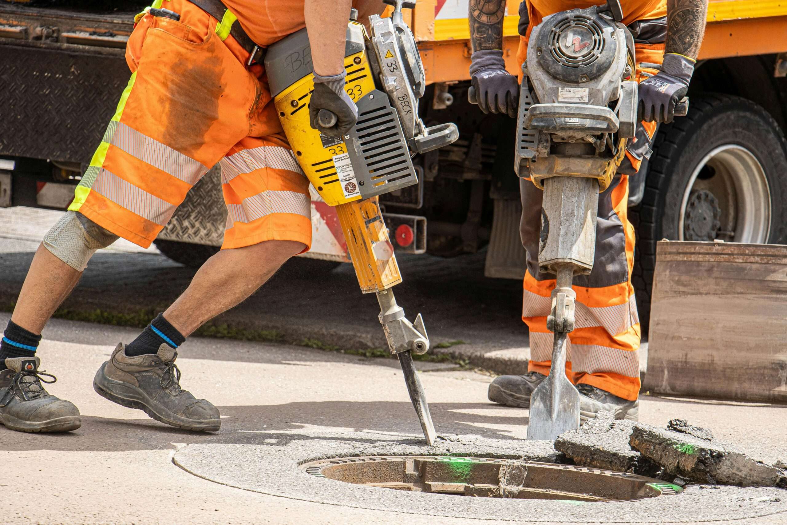 Construction workers use jackhammers on a sewer grate on a road.
