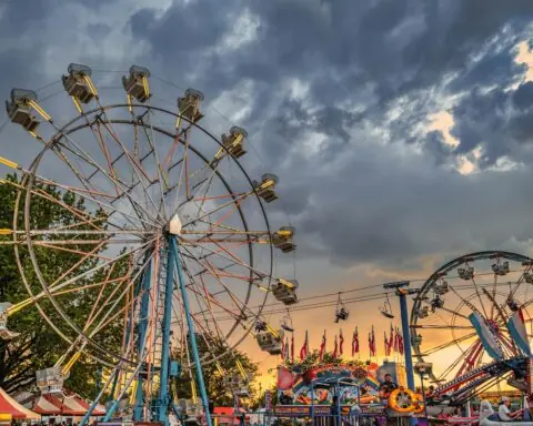 Ferris wheels before a setting sun at a fairground.