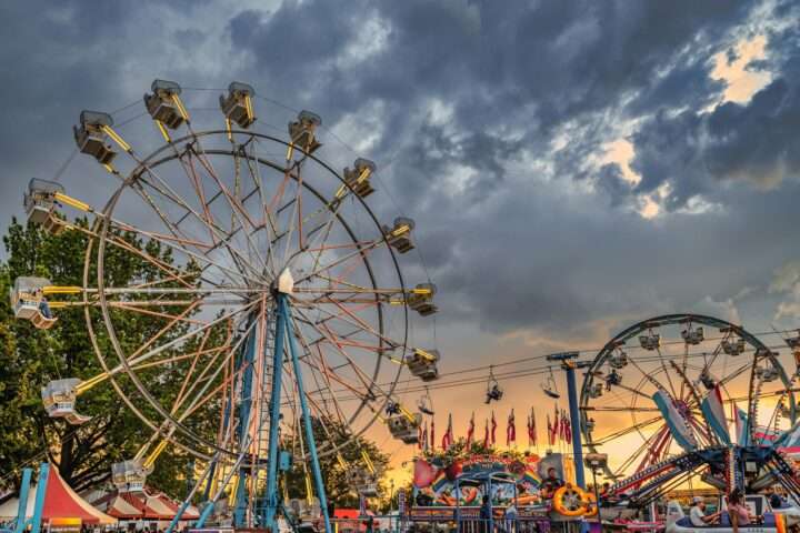 Ferris wheels before a setting sun at a fairground.