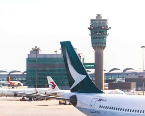 The tail of an airplane before an air traffic control tower at an airport.
