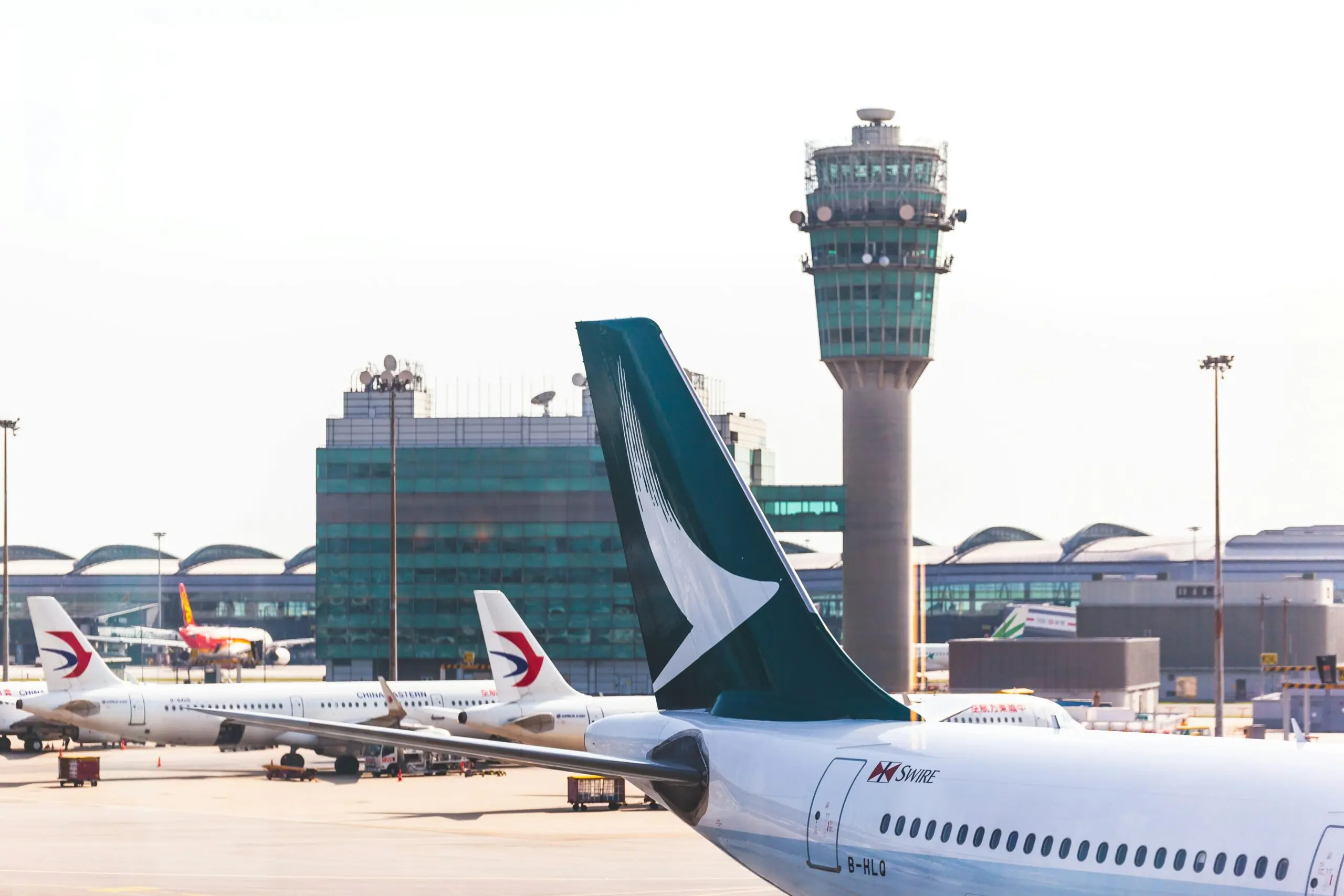 The tail of an airplane before an air traffic control tower at an airport.