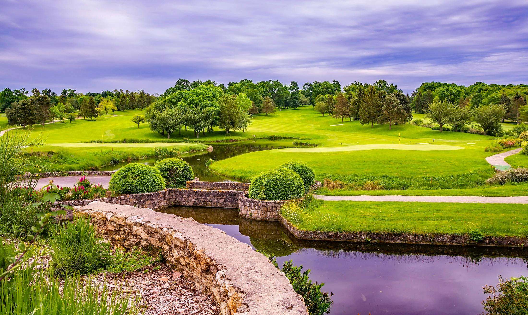 A colorful park with green grass and trees and a water feature.