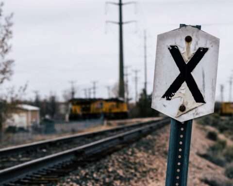 A railroad crossing sign along a track before a grey sky.