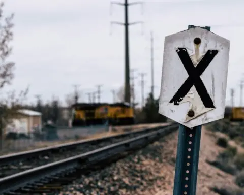 A railroad crossing sign along a track before a grey sky.