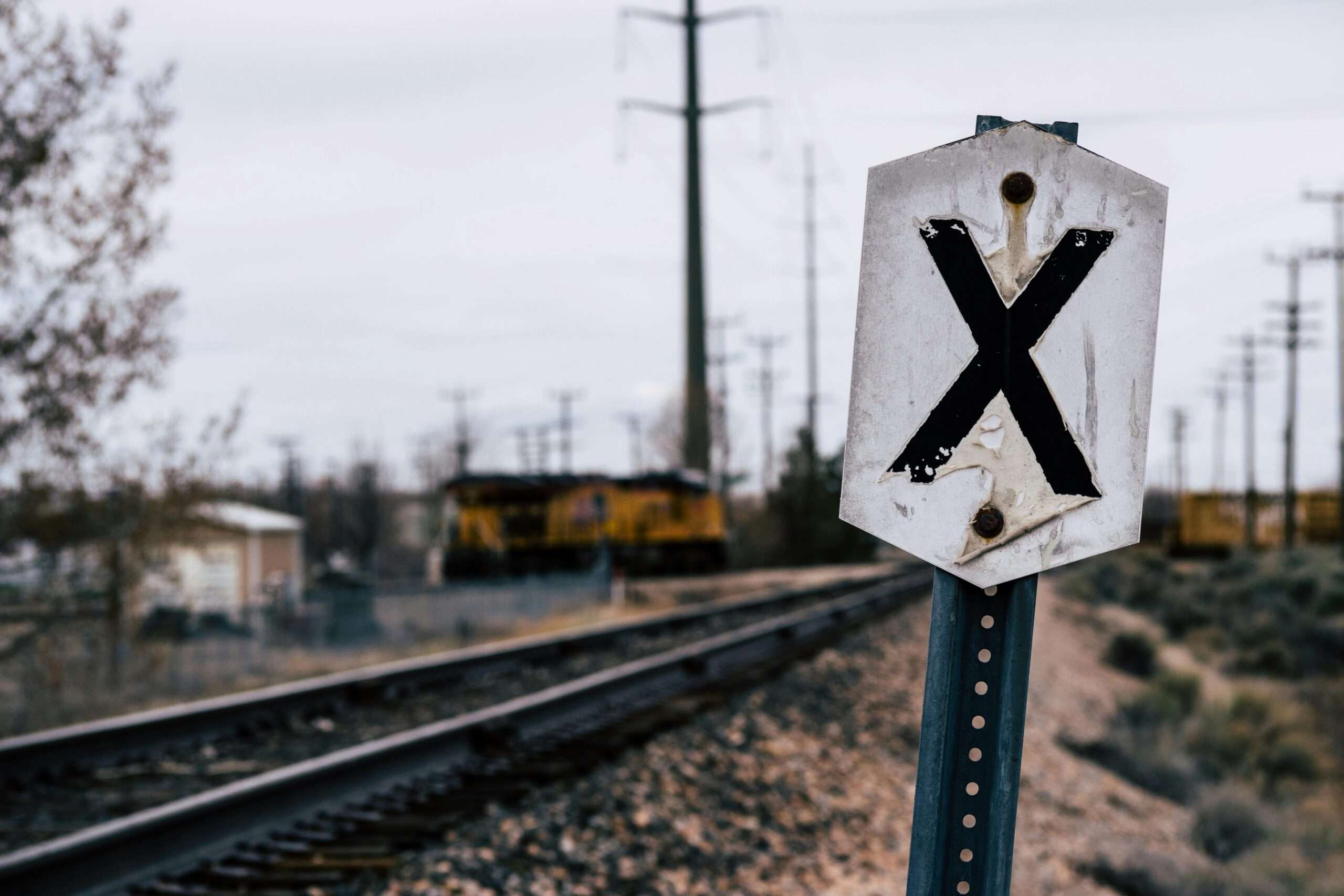 A railroad crossing sign along a track before a grey sky.