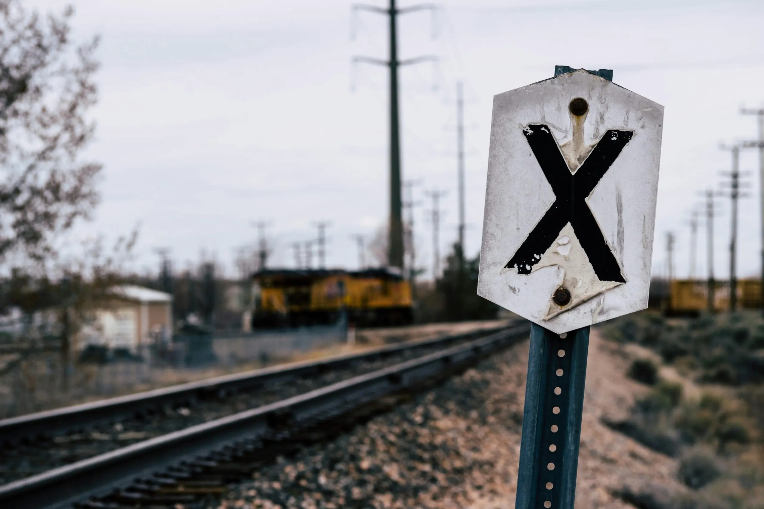 A railroad crossing sign along a track before a grey sky.