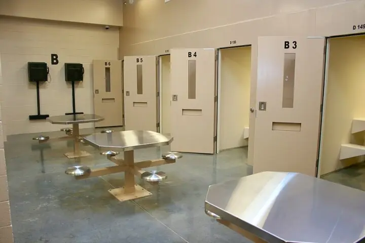 The interior of a jail with several cell doors and tables.