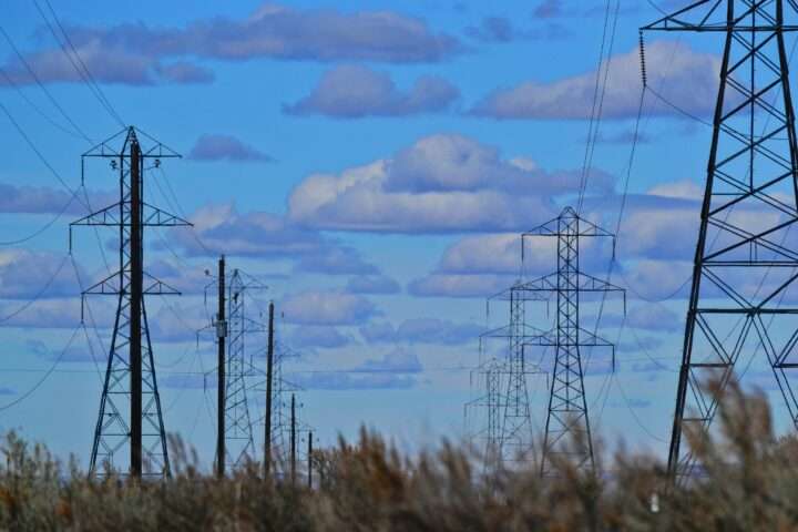 Two rows of electric transmission lines before a blue sky and above a grassy knoll.