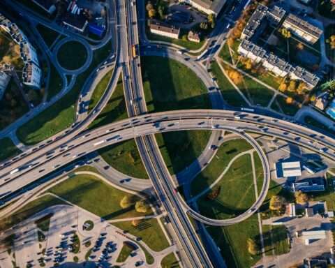 An aerial view of a highway intersection nearby houses, trees and infrastructure.