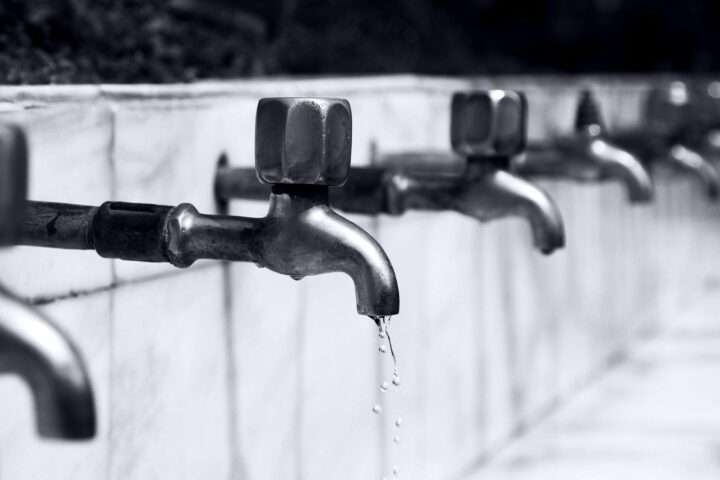 Water faucets in a line along a white wall.