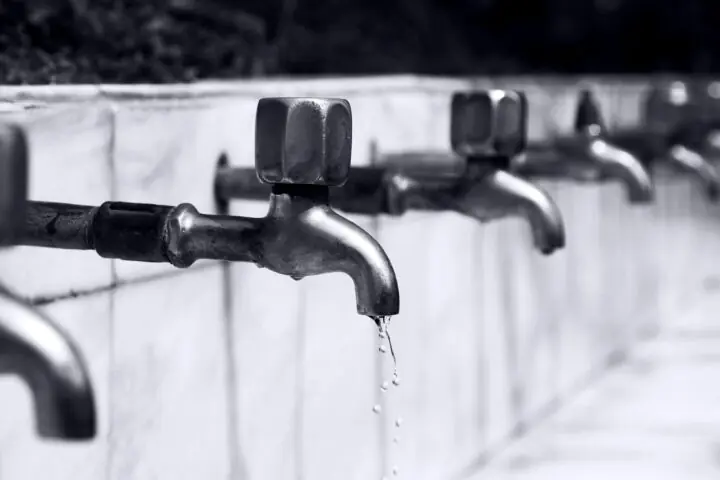 Water faucets in a line along a white wall.