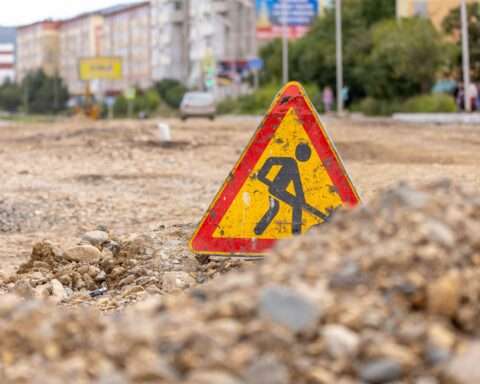 A road work sign on a gravel and dirt patch in an urban area.