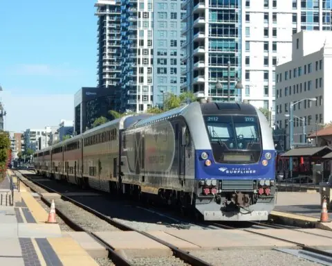 A Pacific Surfliner train in California nearby homes and roads.