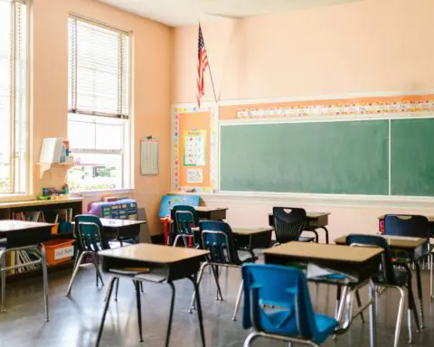 An elementary school classroom with desk and a chalkboard.