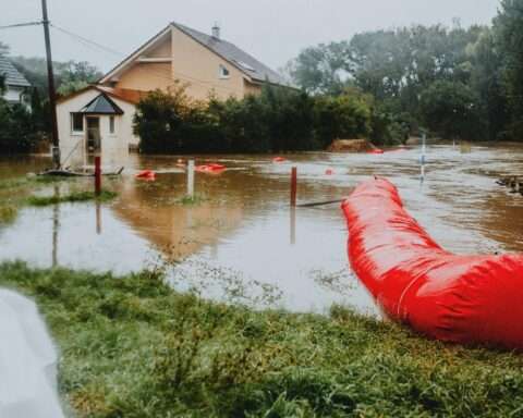 A flood-damaged road submerged nearby a house and greenery.