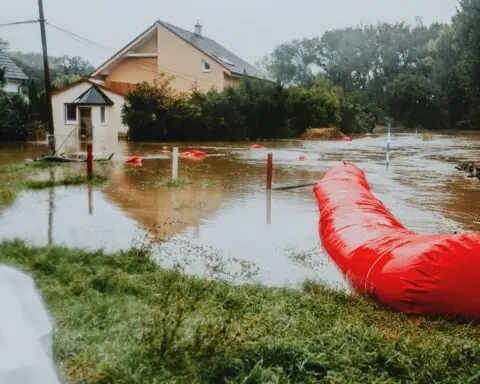 A flood-damaged road submerged nearby a house and greenery.