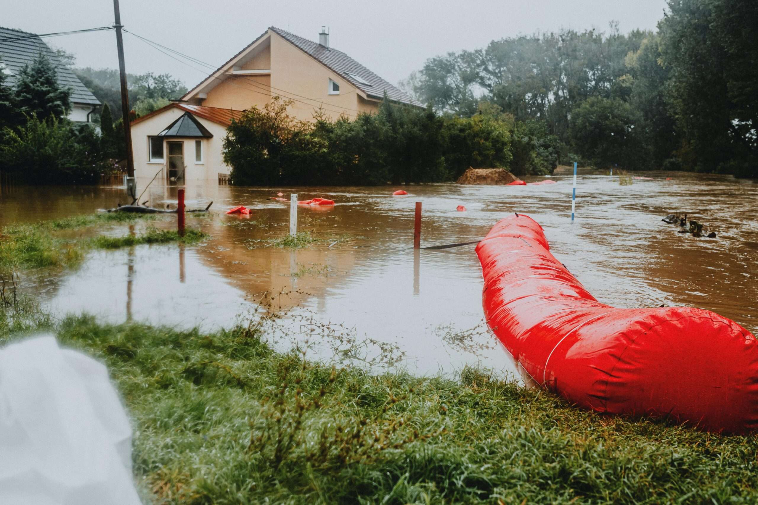A flood-damaged road submerged nearby a house and greenery.