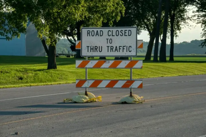 A road construction sign along a road near grass and trees.