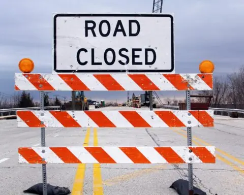 A road closed sign on a construction barricade before a road under construction.